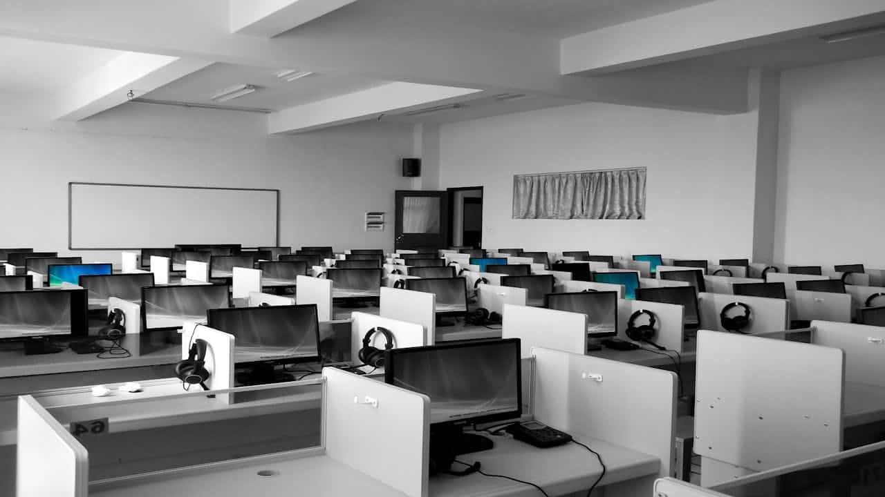 Sala call center moderna con postazioni computer, cuffie e monitor spenti, ambiente vuoto e ordinato.