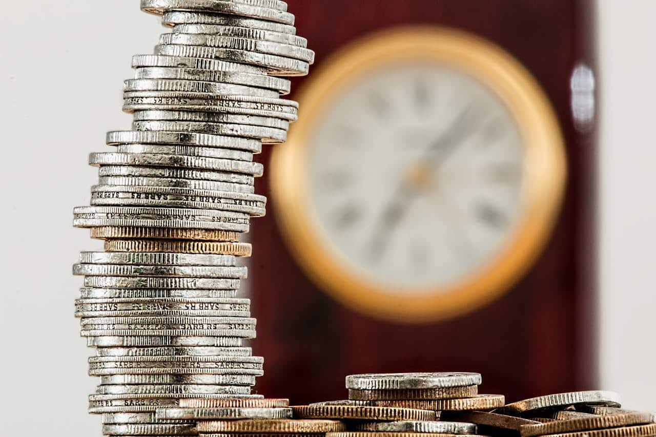 Pile di monete impilate con orologio sfocato sullo sfondo